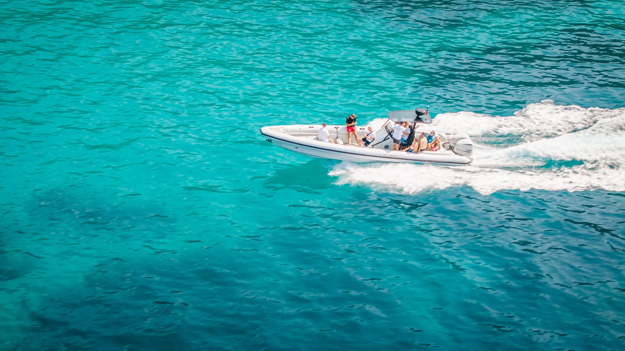 The Beast Boat at speed with guests aboard, throwing a white wake across turquoise water off the Saranda coast
