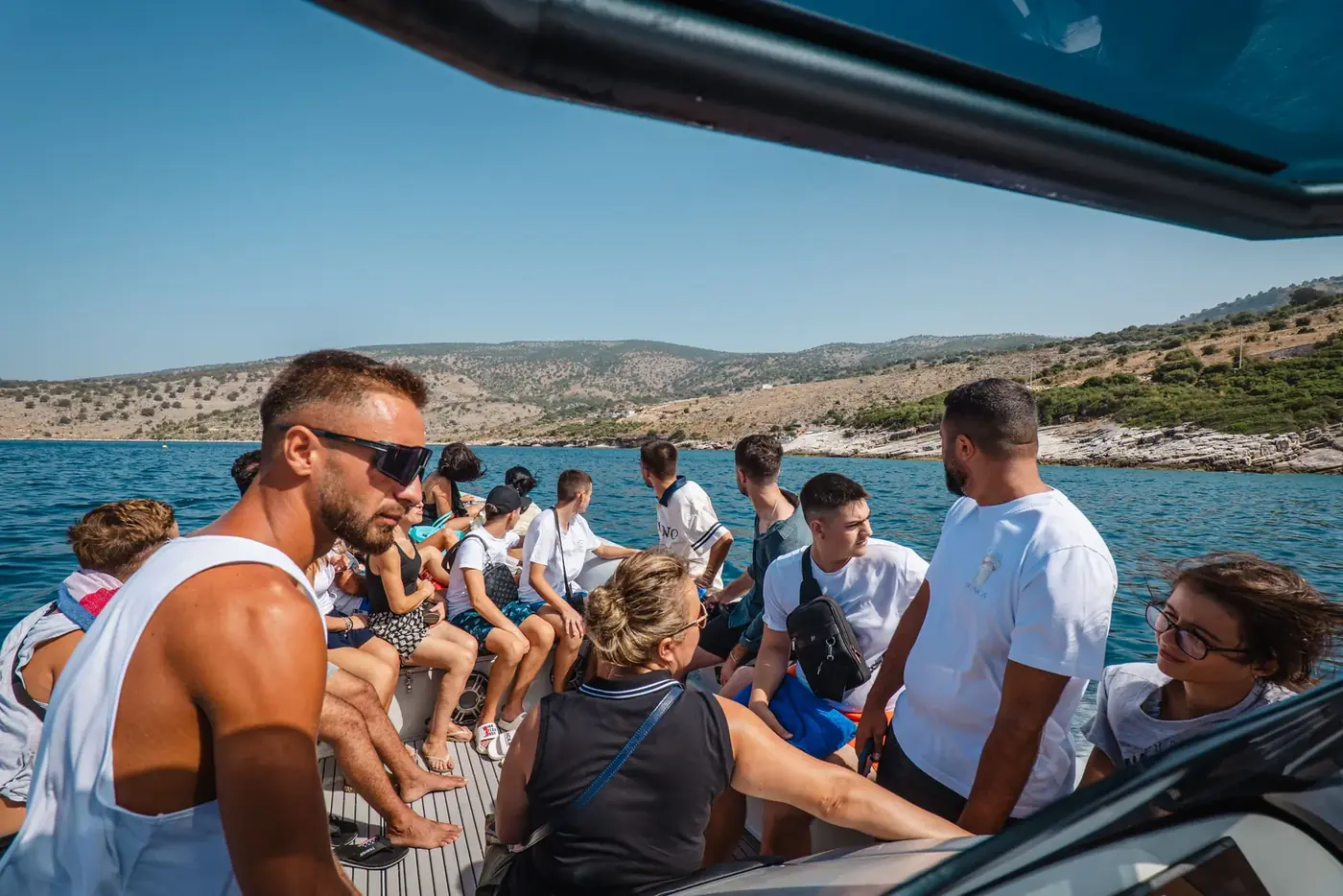 Guests sitting in the sun along the side of the Beast Boat during a Saranda tour